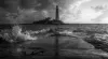 Tall lighthouse on rocky coastline with dramatic waves crashing during stormy weather