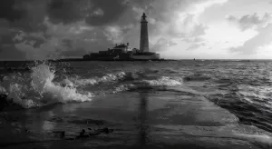 Tall lighthouse on rocky coastline with dramatic waves crashing during stormy weather